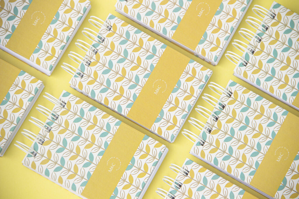 Product Photography for Minico Multiple notepads with yellow, white, and blue leaf abstract design arranged in a pattern on yellow background, photographed by Atlanta product photographer Natalia Tamariz, showcasing colorful stationery for small brands